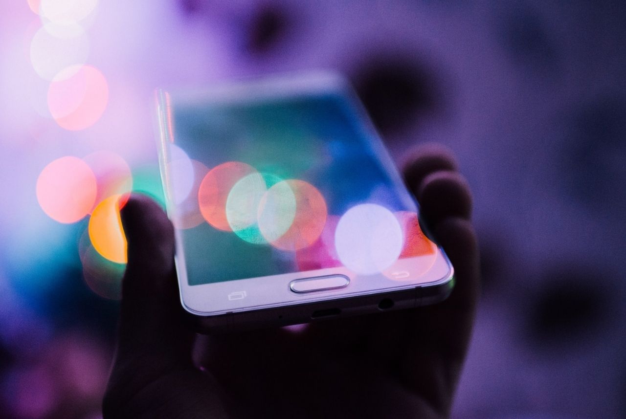 person holding a smartphone with colorful out of focus circles of light overlaying it